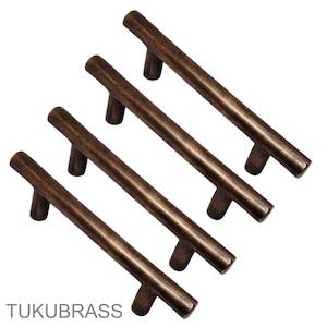 May include: Four bronze-colored cabinet pulls with a T-bar design. The pulls are arranged diagonally against a white background. The text "TUKUBRASS" is visible at the bottom left.