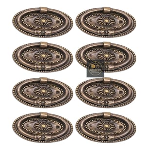 May include: Eight antique brass oval drawer pulls. Each pull has a central floral design, a beaded border, and a curved handle. The pulls are a warm, aged bronze colour, suitable for furniture restoration or new builds.