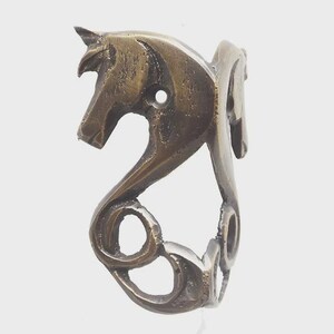 May include: A bronze-coloured ring with a stylised horse head design. The ring has a curved, openwork design with a circular opening near the horse's head. The horse's mane and body flow into the ring's band. A unique piece of jewellery.