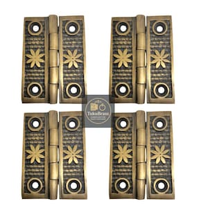 May include: Four antique brass hinges with a floral design. Each hinge has a rectangular shape with a textured surface, decorative flower, and circular accents. The hinges are likely for furniture or cabinetry.