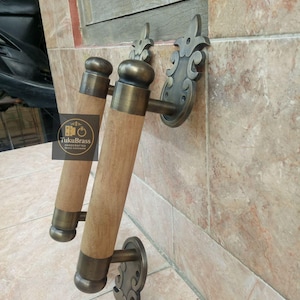 May include: Two brass and wood door handles with decorative wall mounts. The handles have a cylindrical wooden grip with brass accents and a rounded top. The wall mounts feature an ornate, stylized design. The handles are mounted on a tiled wall.