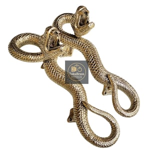 Może przedstawiać: Dwa mosiężne uchwyty do drzwi w kształcie węża z otwartymi pyskami i szczegółowymi łuskami. Uchwyty są w złotym kolorze i mają teksturowaną powierzchnię. Uchwyty są przeznaczone do montażu na drzwiach.