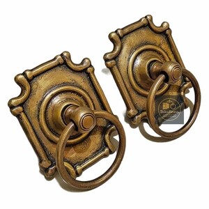 May include: Two antique-style brass drawer pulls. Each pull features a rectangular backplate with ornate detailing and a circular ring handle. The pulls have a warm, aged gold finish, suggesting a vintage aesthetic. The brand name "TukuBrass" is visible.
