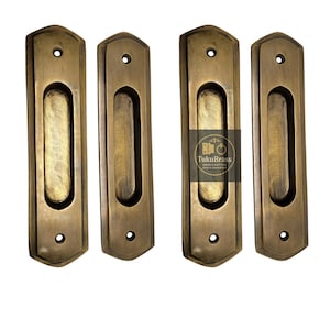 May include: Four antique brass recessed pulls. Each pull has a rectangular shape with a rounded top and bottom, and a central oval indentation for gripping. The pulls are a warm, aged brass colour, suggesting vintage hardware.