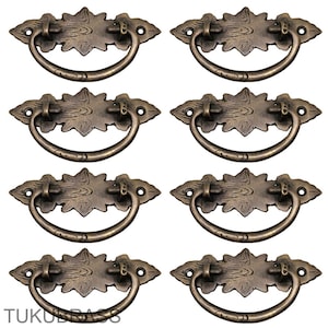 May include: Eight antique bronze drawer pulls. Each pull has a decorative backplate with a floral design and a curved handle. The pulls are made of metal and have a vintage aesthetic.