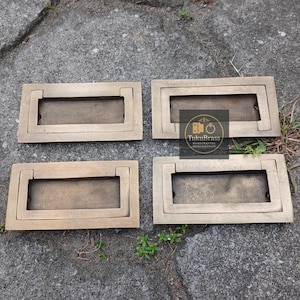 Op de afbeelding: Vier rechthoekige messing lade grepen met een verzonken midden en een verhoogde rand. De grepen zijn gerangschikt op een grijs stenen oppervlak. De afbeelding bevat de tekst "TukuBrass HANDCRAFTED BRASS HARDWARE".