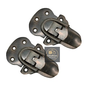 Puede incluir: Dos pestillos metálicos de estilo antiguo con acabado bronce oscuro. Cada pestillo tiene una base rectangular con múltiples orificios para tornillos y un asa curva con bisagras. Los pestillos son probablemente para un cofre.