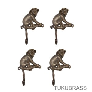 May include: Four bronze-colored monkey-shaped wall hooks. Each hook features a monkey sitting on a branch with a hook extending downwards. The hooks are made of metal and are suitable for hanging items. The text "TUKUBRASS" is at the bottom.
