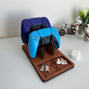 May include: A wooden gaming controller stand with two controllers, one blue and one purple. The stand also holds USB drives, earbuds, and a charging case. The stand has the text "Chef TG" engraved on it.