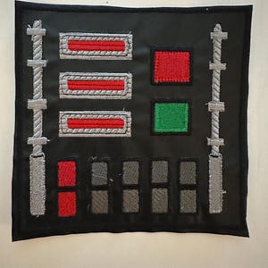 May include: Black square patch with embroidered details. Features three horizontal red rectangles, a red square, a green square, and several grey rectangles. Two vertical grey columns with rope-like designs flank the sides.