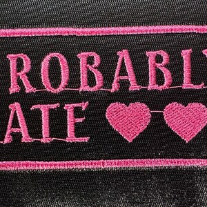 May include: Black patch with pink embroidered text that reads "PROBABLY LATE" with two pink hearts. The text and hearts are inside a pink rectangular border.