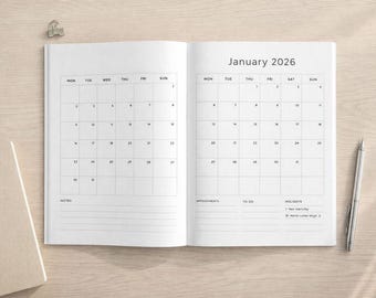 Puede incluir: Cuaderno abierto con un calendario de enero de 2026. El calendario está en formato de cuadrícula con los días de la semana en la parte superior. Un bolígrafo plateado descansa en la página derecha. También se ve un clip y un cuaderno.