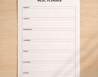 Puede incluir: Una hoja blanca de planificador de comidas con las palabras "MEAL PLANNER" en la parte superior. El planificador tiene secciones para cada día de la semana, con líneas para escribir planes de comidas. El fondo es de madera clara.