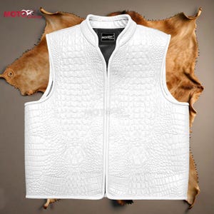 Puede incluir: Un chaleco blanco sin mangas con un patrón texturizado similar al de un cocodrilo. El chaleco tiene un cuello alto y una cremallera de largo completo. El forro interior es negro. El chaleco se muestra sobre un fondo marrón.