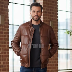 Puede incluir: Chaqueta bomber de cuero marrón con diseño acolchado. La chaqueta tiene cierre de cremallera, puños y dobladillo de canalé. El modelo lleva debajo una camiseta gris oscuro. La chaqueta es de estilo clásico.