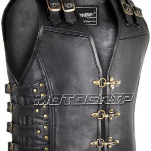 Puede incluir: Chaleco de cuero negro con múltiples correas, hebillas y remaches. El chaleco tiene un diseño de cuello en V y presenta el logotipo "MOTO GRIP". El chaleco está diseñado para motociclistas.