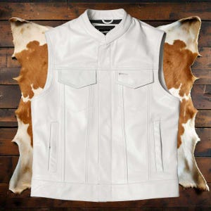 Może przedstawiać: Biała skórzana kamizelka z kołnierzem mandaryńskim i dwiema kieszeniami na piersi. Kamizelka ma pionowe przeszycia i dwie dolne kieszenie. Bezrękawnik ma klasyczny styl motocyklowy.