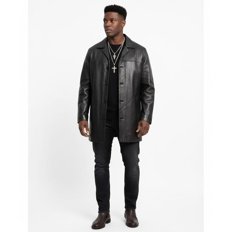 May include: A black leather coat with a button-up front, worn with black jeans and brown boots. The coat has a classic, tailored design. The person is wearing a silver cross necklace.