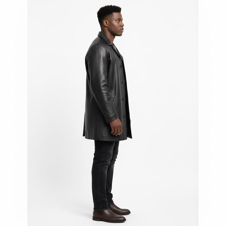 May include: A black leather coat with a button-up front and a collared neckline. The coat is knee-length and worn with black jeans and brown leather boots. The coat appears to be made of a smooth, high-quality leather.