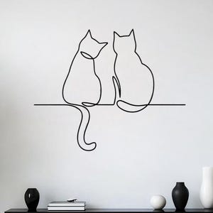 May include: A black line drawing of two cats sitting side-by-side on a shelf. The cats are depicted in a minimalist style, with a single continuous line forming their outlines. The shelf is also a black line. The background is a white wall.