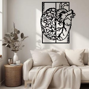 May include: Black metal wall art depicting a brain and a heart, side-by-side within a rectangular frame. The words "THINK" and "FEEL" are vertically placed on the frame. The artwork is displayed above a white sofa with pillows and a blanket.