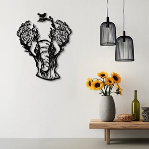 May include: Black metal wall art of an elephant with tree-like features. The elephant's body is formed by the trunk, while the ears are branches. A small bird sits atop the tree. The art is displayed on a white wall.