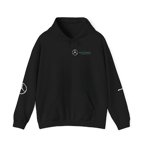 May include: Black hooded sweatshirt with a front pocket and drawstring. Features the Mercedes-Benz logo on the chest, left sleeve, and the AMG logo on the right sleeve. The text "PETRONAS" is above the Mercedes-Benz logo.