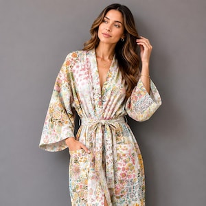 May include: A long-length robe featuring a vibrant, multi-colored floral pattern on a white background. The garment includes wide, three-quarter length sleeves, a V-neckline, two front patch pockets, and a matching fabric tie belt at the waist.