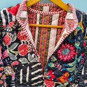 May include: A quilted jacket featuring a black base with a vibrant floral pattern in shades of red, pink, and green. The interior lining displays a vertical striped design in pink, green, and white, finished with a red and white striped trim.
