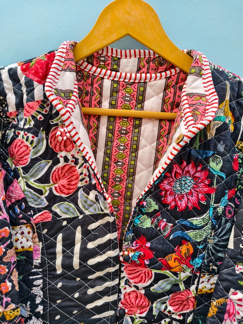 May include: A quilted jacket featuring a black base with a vibrant floral pattern in shades of red, pink, and green. The interior lining displays a vertical striped design in pink, green, and white, finished with a red and white striped trim.
