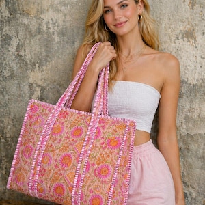 May include: A large tote bag with a floral pattern in shades of pink and orange. The bag has pink handles and trim. The background is a textured, neutral-toned wall.