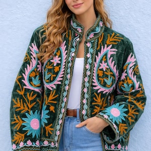 Può includere: Giacca in velluto verde scuro con ricami floreali colorati in rosa, arancione e blu. La giacca presenta un collo alto e una cintura marrone. Il ricamo crea un design a forma di paisley, aggiungendo un tocco bohémien all'indumento.
