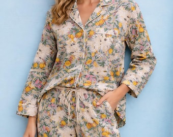 May include: A two-piece pajama set featuring a long-sleeved button-down shirt with a collar and matching drawstring pants. The fabric is light gray with a colorful floral print consisting of yellow, pink, and white flowers and green leaves.