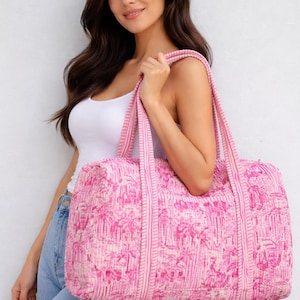Puede incluir: Bolsa de lona rosa y blanca estampada con asas a juego. La bolsa presenta un diseño tropical repetido. La bolsa la sostiene una persona que lleva una camiseta sin mangas blanca y vaqueros azules.