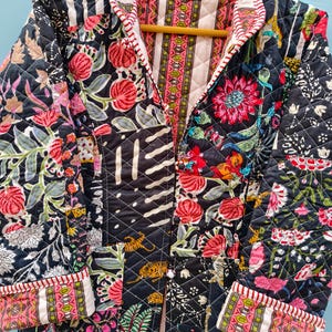 May include: A quilted jacket featuring a patchwork design with a black base and vibrant floral, tiger, and striped patterns in pink, green, and white. The garment has long sleeves, a front button closure, and a red and white striped trim along the edges.