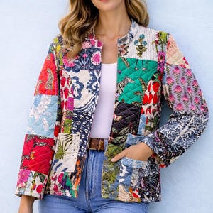 May include: A colourful patchwork jacket featuring floral, animal, and geometric designs in various shades. The jacket has a collarless design, long sleeves, and two pockets. The model is wearing blue jeans and a white top.