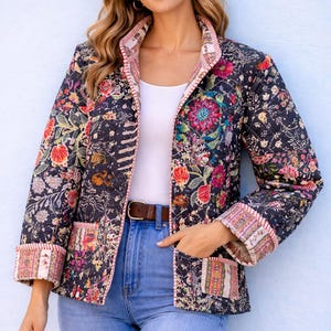 May include: A quilted jacket featuring a dark navy base with a vibrant, multi-coloured floral print. The jacket has long sleeves with folded cuffs, a front button closure, and two patch pockets. The edges are finished with a striped trim detail.
