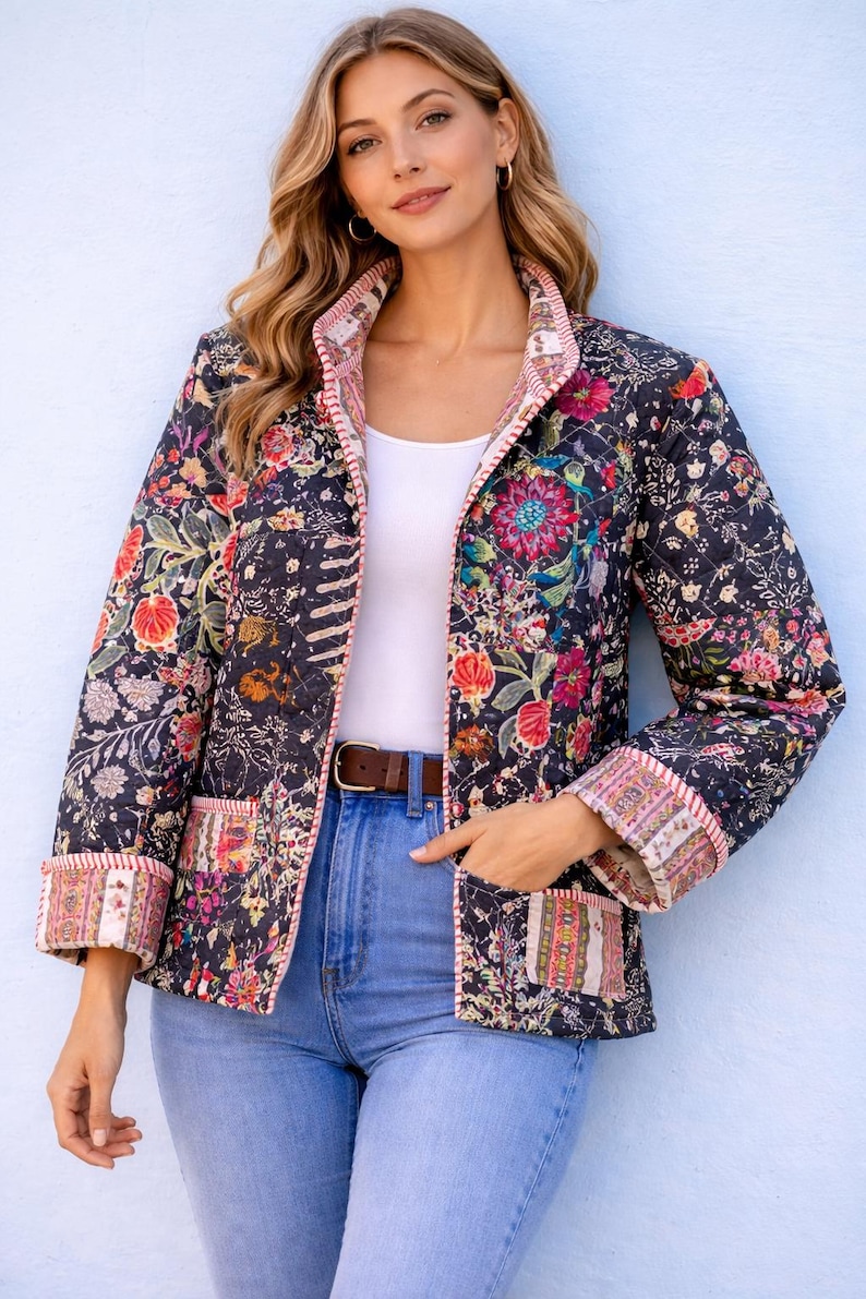 May include: A quilted jacket featuring a dark navy base with a vibrant, multi-coloured floral print. The jacket has long sleeves with folded cuffs, a front button closure, and two patch pockets. The edges are finished with a striped trim detail.