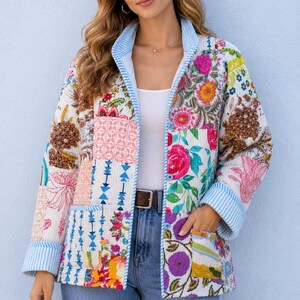 Könnte beinhalten: Bunte Patchwork-Jacke mit floralen Mustern in Rosa, Blau und Gelb. Die Jacke hat einen blau-weiß gestreiften Besatz an Kragen und Manschetten. Die Jacke wird mit einer blauen Jeans getragen.