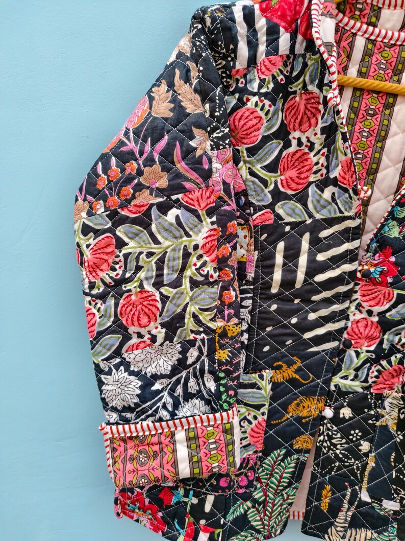 May include: A quilted jacket featuring a patchwork design with black, pink, and green floral and animal patterns. The garment has long sleeves with folded cuffs, a front opening, and a diamond-stitched texture throughout the fabric.