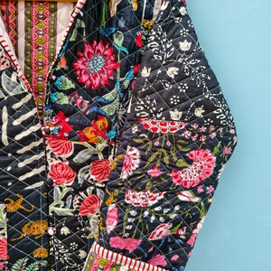 May include: A quilted jacket featuring a dark navy background with a vibrant floral and tiger print in shades of pink, orange, and green. The garment has a V-neckline, long sleeves with folded cuffs, and a contrasting striped trim along the edges.