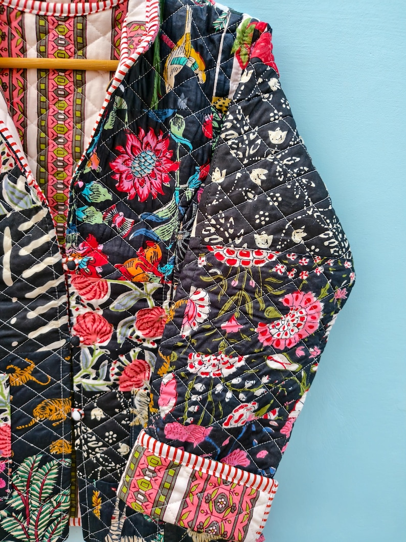 May include: A quilted jacket featuring a dark navy background with a vibrant floral and tiger print in shades of pink, orange, and green. The garment has a V-neckline, long sleeves with folded cuffs, and a contrasting striped trim along the edges.