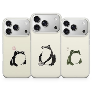 May include: Three phone cases with a cream background and frog illustrations. The frogs are depicted in a minimalist style, with black and green ink drawings. Each case features a different frog design, with Japanese text.