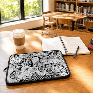 Könnte beinhalten: Eine rechteckige Laptoptasche mit einer detaillierten schwarz-weißen Tuschezeichnung aus verschiedenen Blumen, wirbelnden Mustern und organischen Formen. Die Tasche hat einen schwarzen Reißverschluss und einen schwarzen Rand.
