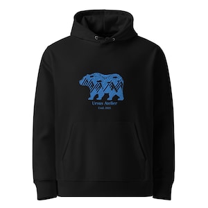 Puede incluir: Sudadera con capucha negra con un diseño de oso azul. El oso está hecho de líneas y formas azules. El texto "Ursus Atelier Est. 2025" está debajo. La sudadera tiene capucha y bolsillo delantero.