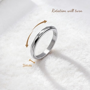 May include: A silver-colored ring with a faceted design. The ring is 3mm wide and has the text "Rotation will turn" with an arrow indicating the ring's rotating feature. The ring is displayed on a white, textured surface.