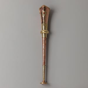May include: A decorative staff with a copper and gold finish. The top section is copper with gold accents and a small red gem. The staff has a long, slender copper shaft and a gold base.