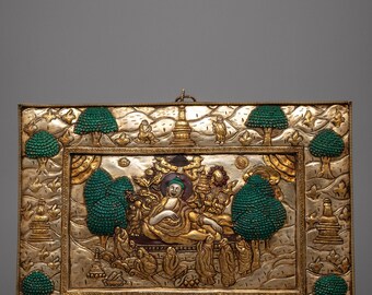 May include: A rectangular, silver-toned relief sculpture with gold accents. The central image depicts a seated figure surrounded by smaller figures and trees with green textured foliage. The border features additional trees and decorative elements.