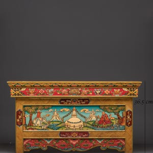 Può includere: Un mobile in legno intagliato a mano con dettagli intricati. Il mobile è largo 65 cm e alto 36,5 cm. Presenta un pannello centrale con una scena paesaggistica e motivi floreali e geometrici ornati in rosso, oro e blu.