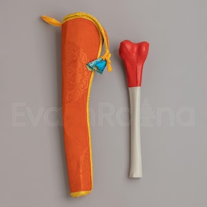 May include: An orange sheath with gold trim and a decorative blue and yellow tassel next to a red and white ceremonial item. The sheath has a detailed pattern. The ceremonial item has a heart-shaped top.